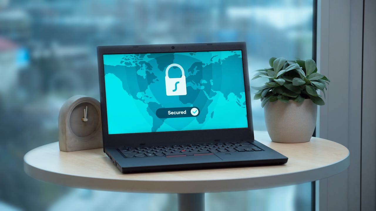 Services Laptop displaying a security lock icon on a table with a potted plant and clock.